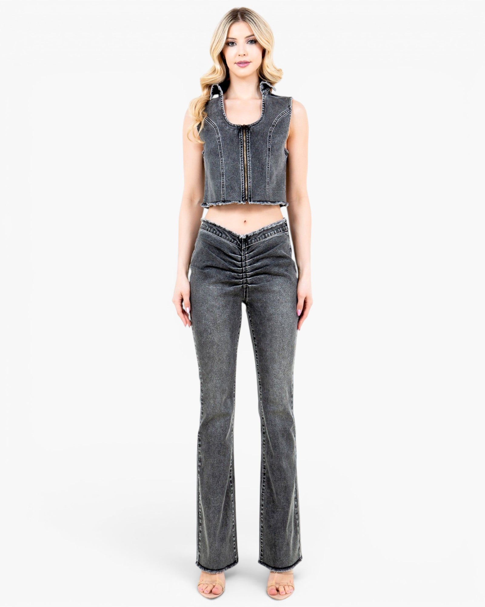 A woman modeling a dark gray washed denim set consisting of a sleeveless cropped vest and matching high-waisted flared jeans with front ruching, against a plain white studio background.