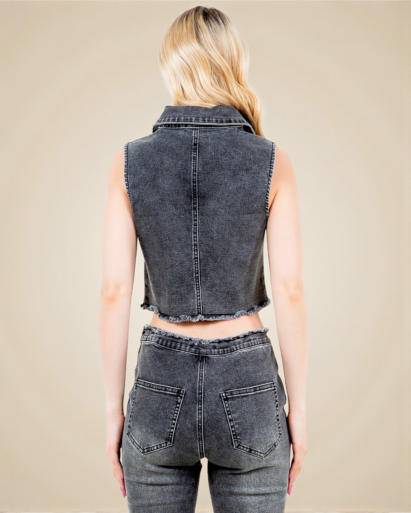 Person wearing a sleeveless denim vest and jeans on a beige background