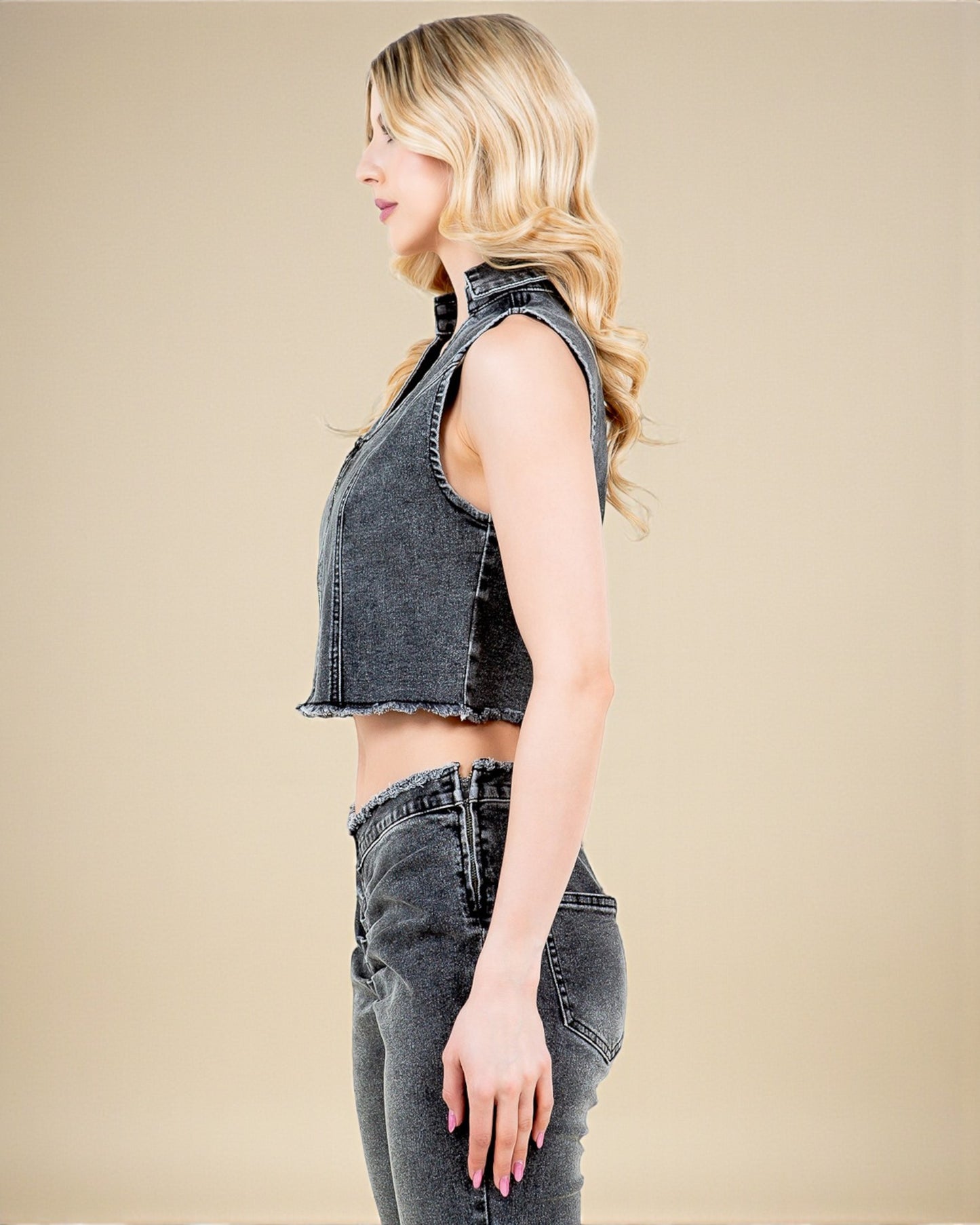 Woman wearing a sleeveless denim top and jeans on a beige background