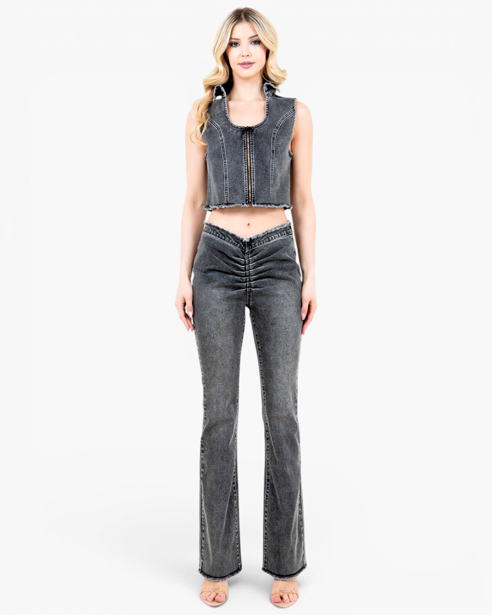 A woman modeling a dark gray washed denim set consisting of a sleeveless cropped vest and matching high-waisted flared jeans with front ruching, against a plain white studio background.