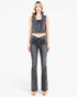 A woman modeling a dark gray washed denim set consisting of a sleeveless cropped vest and matching high-waisted flared jeans with front ruching, against a plain white studio background.