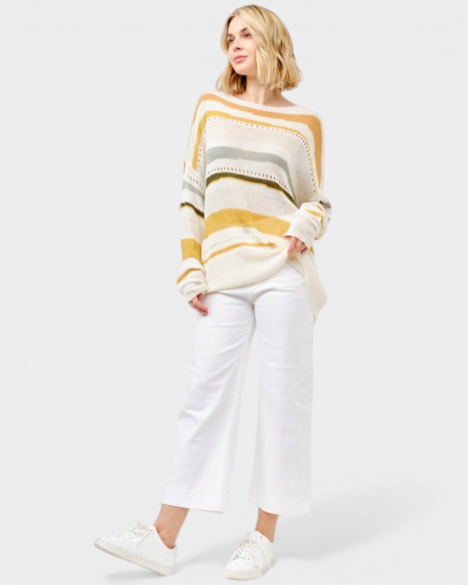 Woman wearing a striped sweater and white pants on a plain background