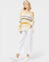 Woman wearing a striped sweater and white pants on a plain background