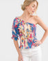Woman wearing a colorful one-shoulder top against a white background