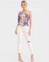 Woman wearing a colorful floral top and white pants on a white background