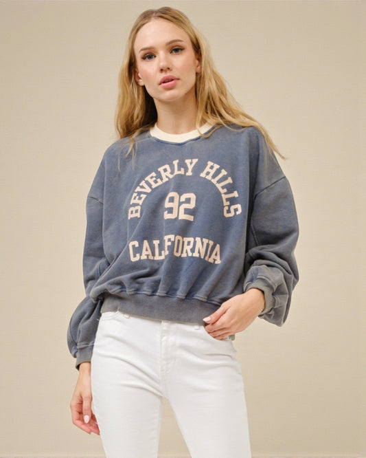 Woman wearing a blue sweatshirt with 'Beverly Hills 92 California' text on a beige background