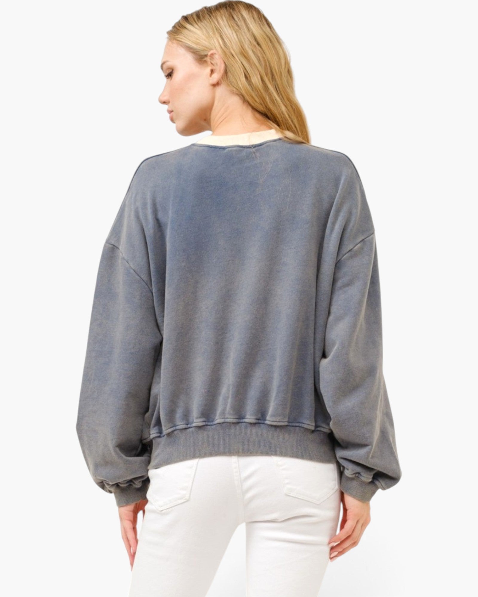 A woman shown from the back wearing a faded slate blue-gray crewneck sweatshirt and white pants, photographed against a clean white background.