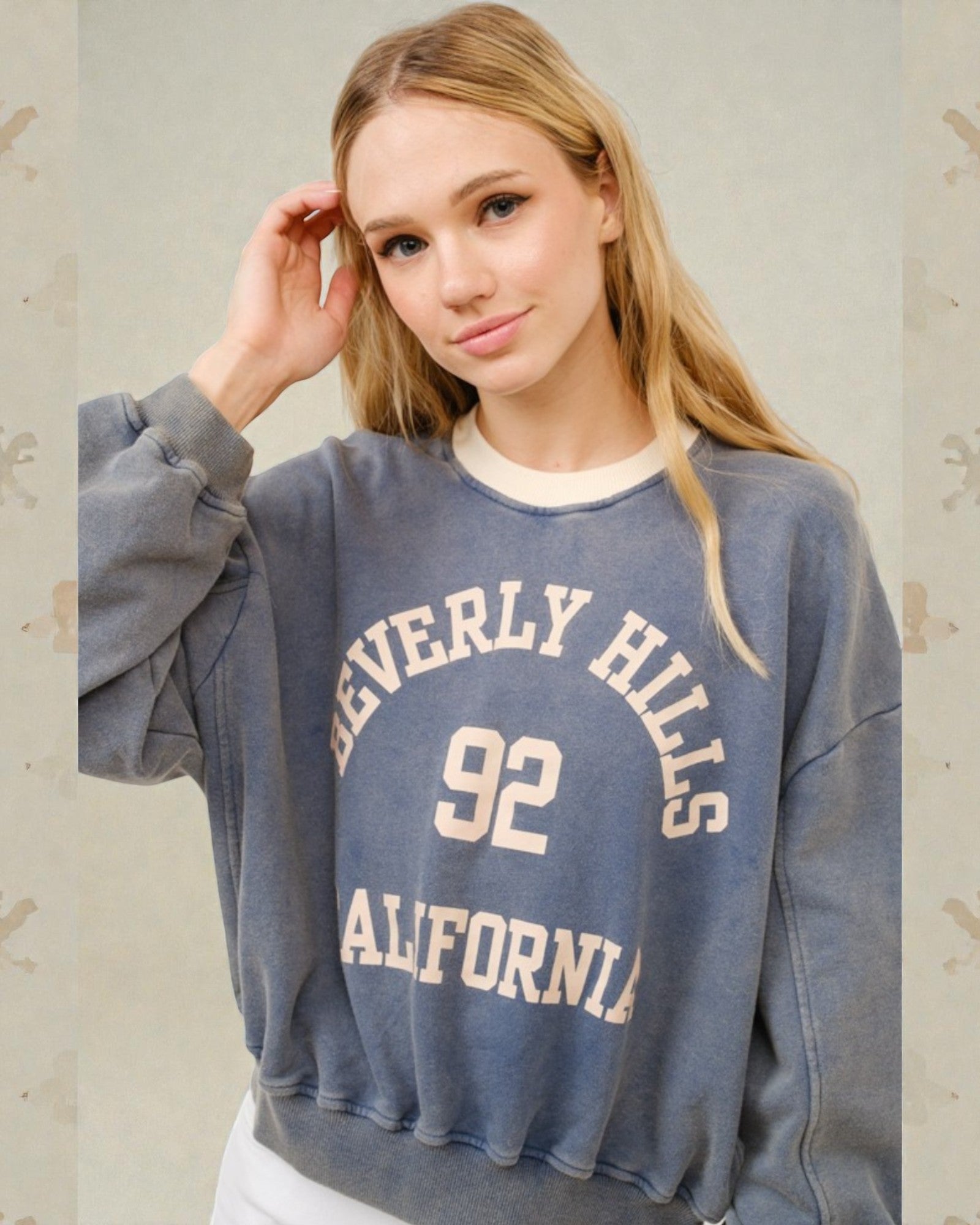Woman wearing a blue sweatshirt with 'Beverly Hills 92 California' text on a light background