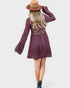 Woman wearing a purple dress with long sleeves and a brown hat on a white background