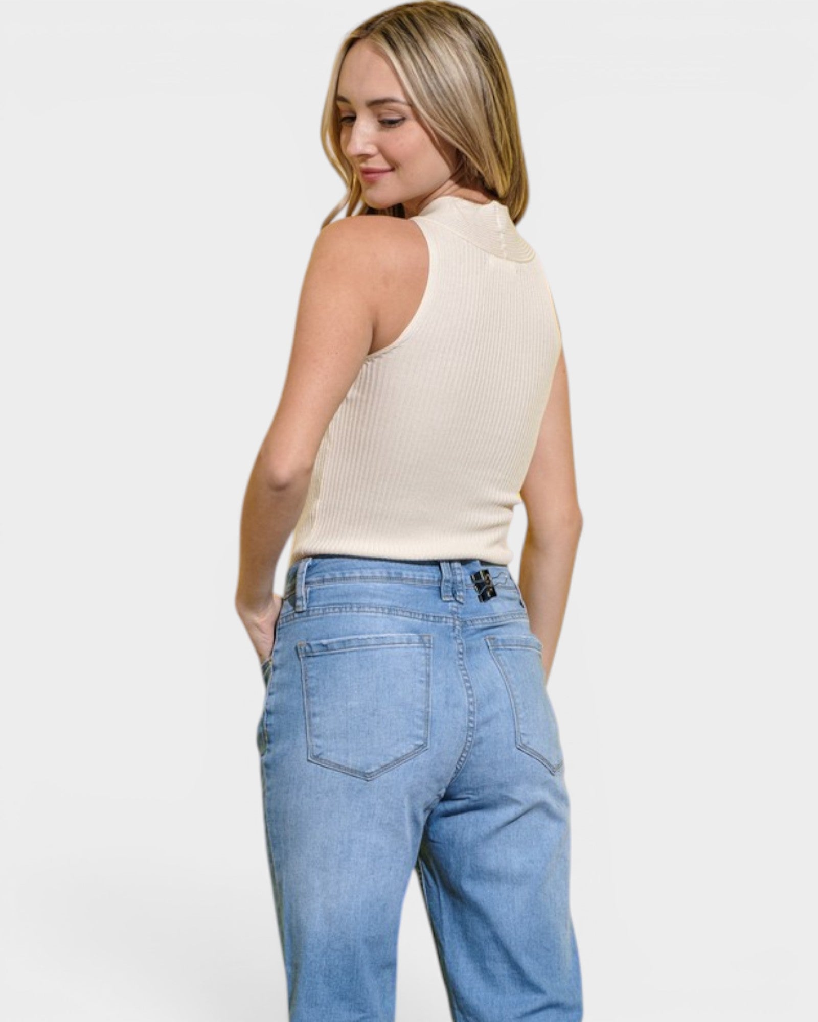 Woman wearing a beige sleeveless top and light blue jeans on a white background