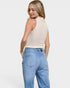 Woman wearing a beige sleeveless top and light blue jeans on a white background