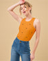Woman wearing an orange tank top with black patterns and blue jeans on a beige background