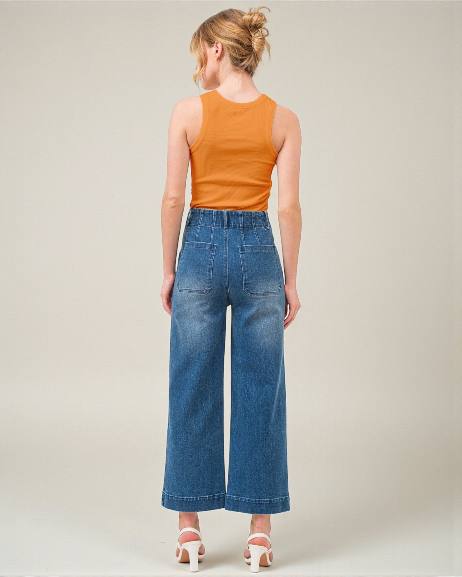 Woman wearing a mustard yellow sleeveless top and blue high-waisted jeans on a plain background