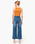 A woman shown from the back wearing a bright orange sleeveless top and high-waisted blue wide-leg denim jeans, paired with white heeled sandals, against a plain white studio background.
