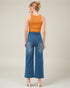 Woman wearing a mustard yellow sleeveless top and blue high-waisted jeans on a plain background