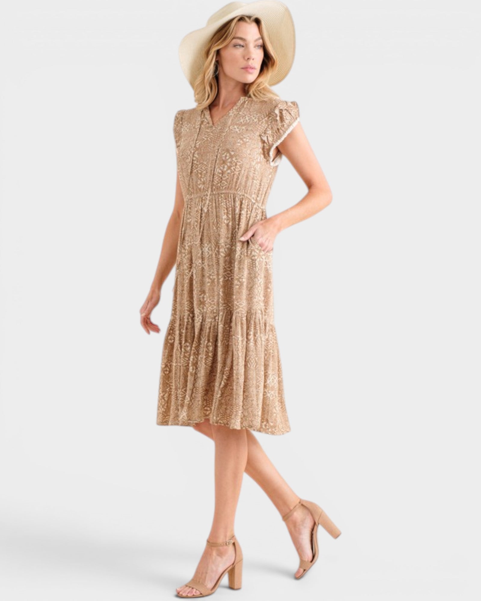 Woman wearing a gold patterned dress and beige hat on a white background
