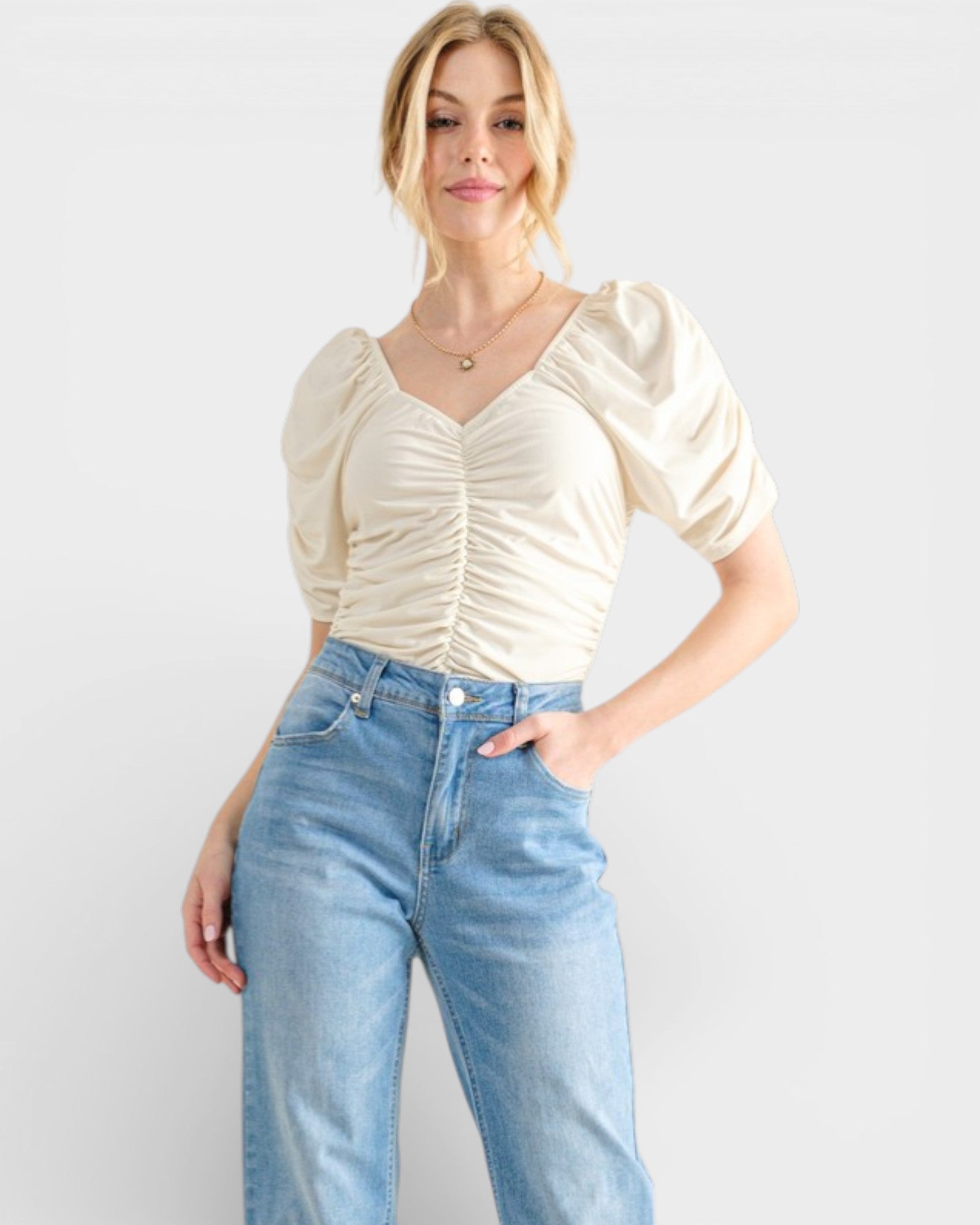Woman wearing a cream blouse and blue jeans against a white background