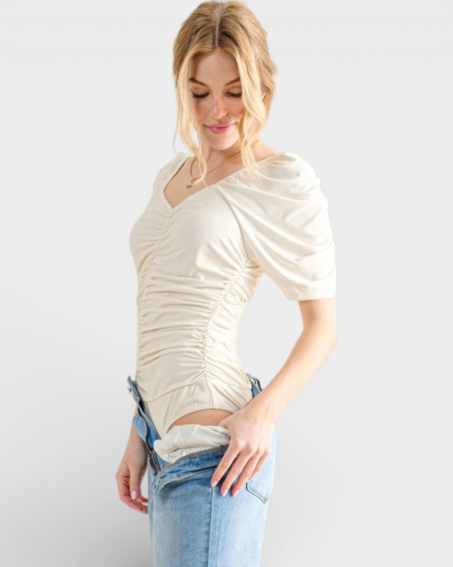 Woman wearing a cream-colored top and blue jeans on a white background