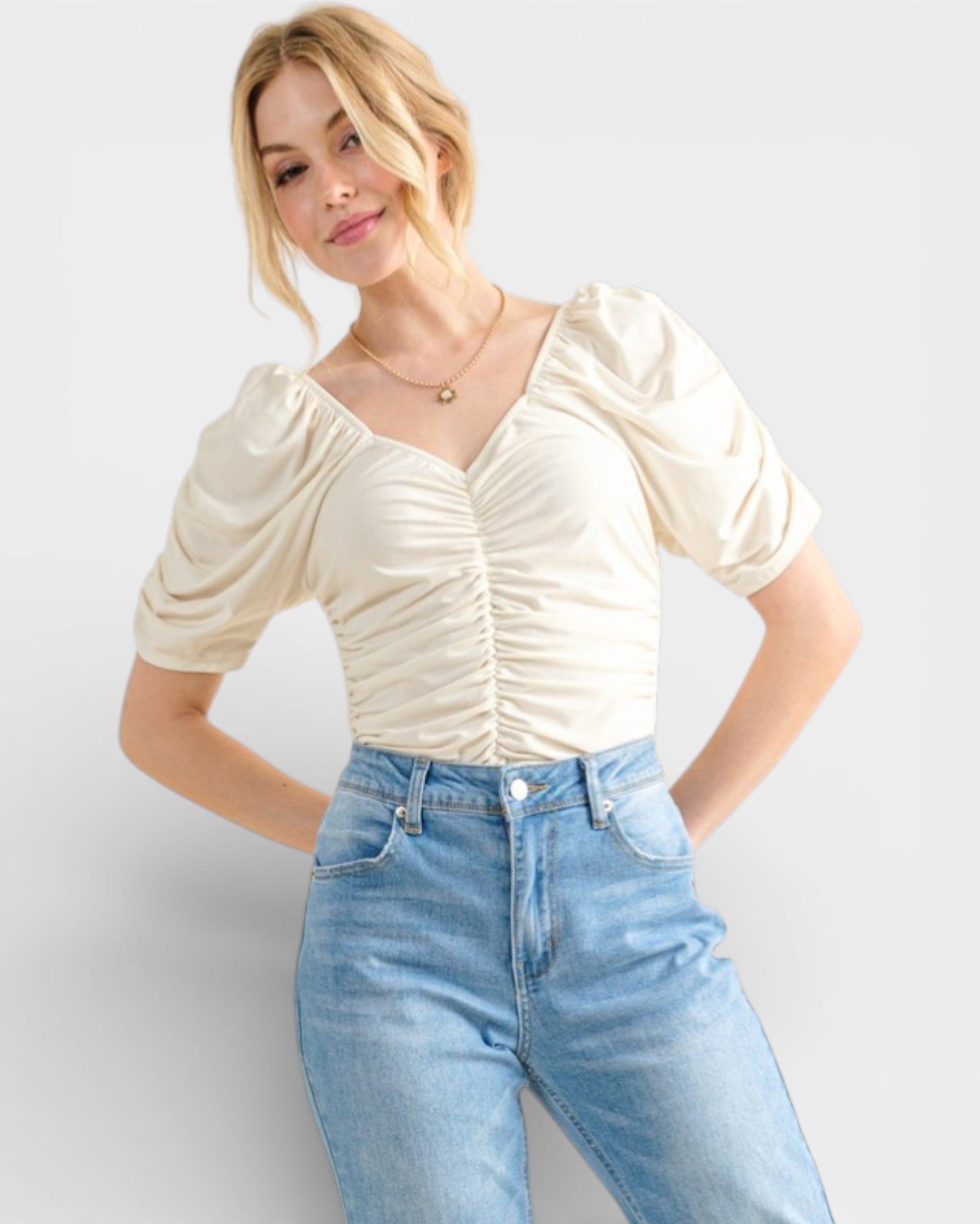 Woman wearing a cream top and blue jeans against a white background