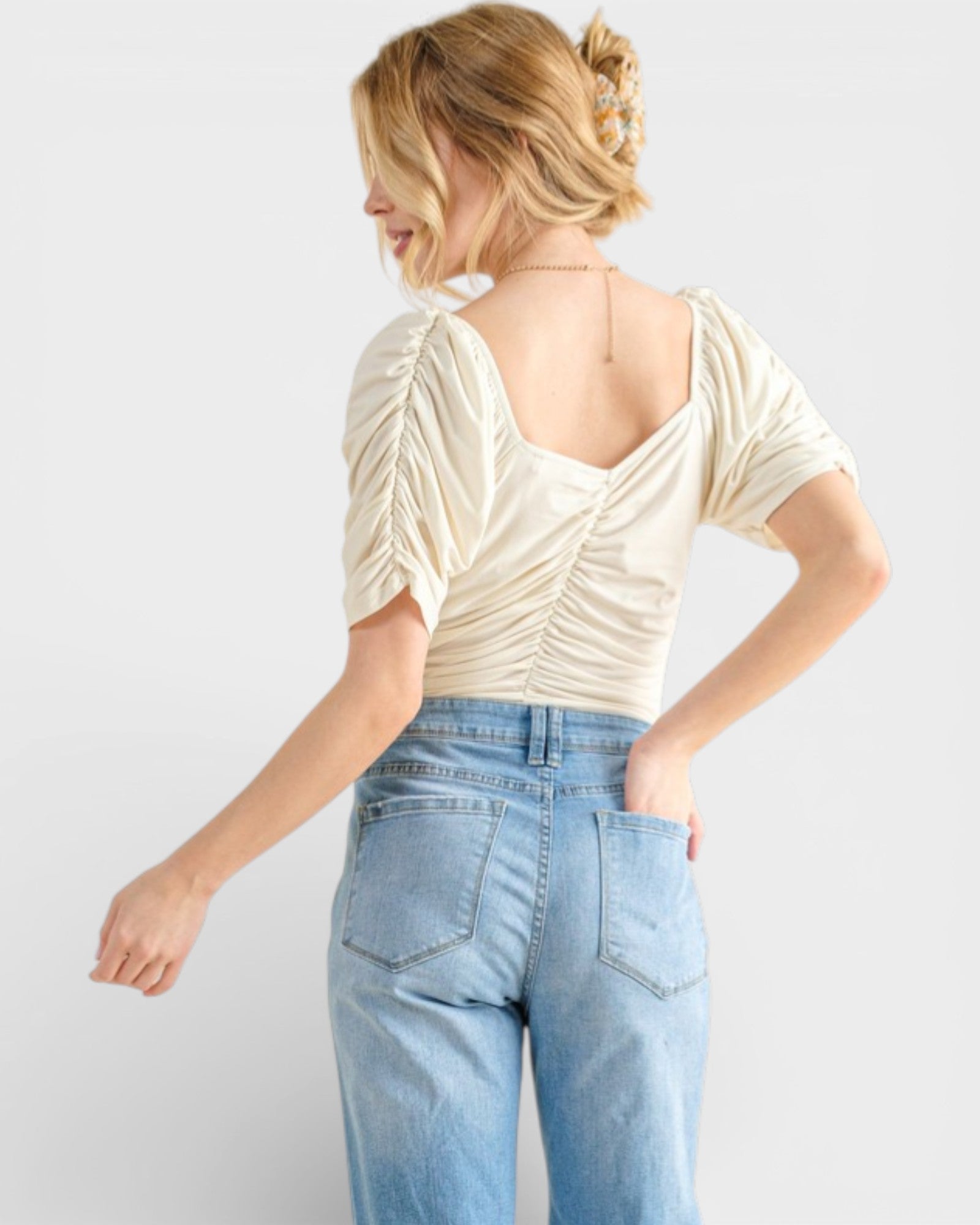 Woman wearing a cream top and blue jeans on a white background