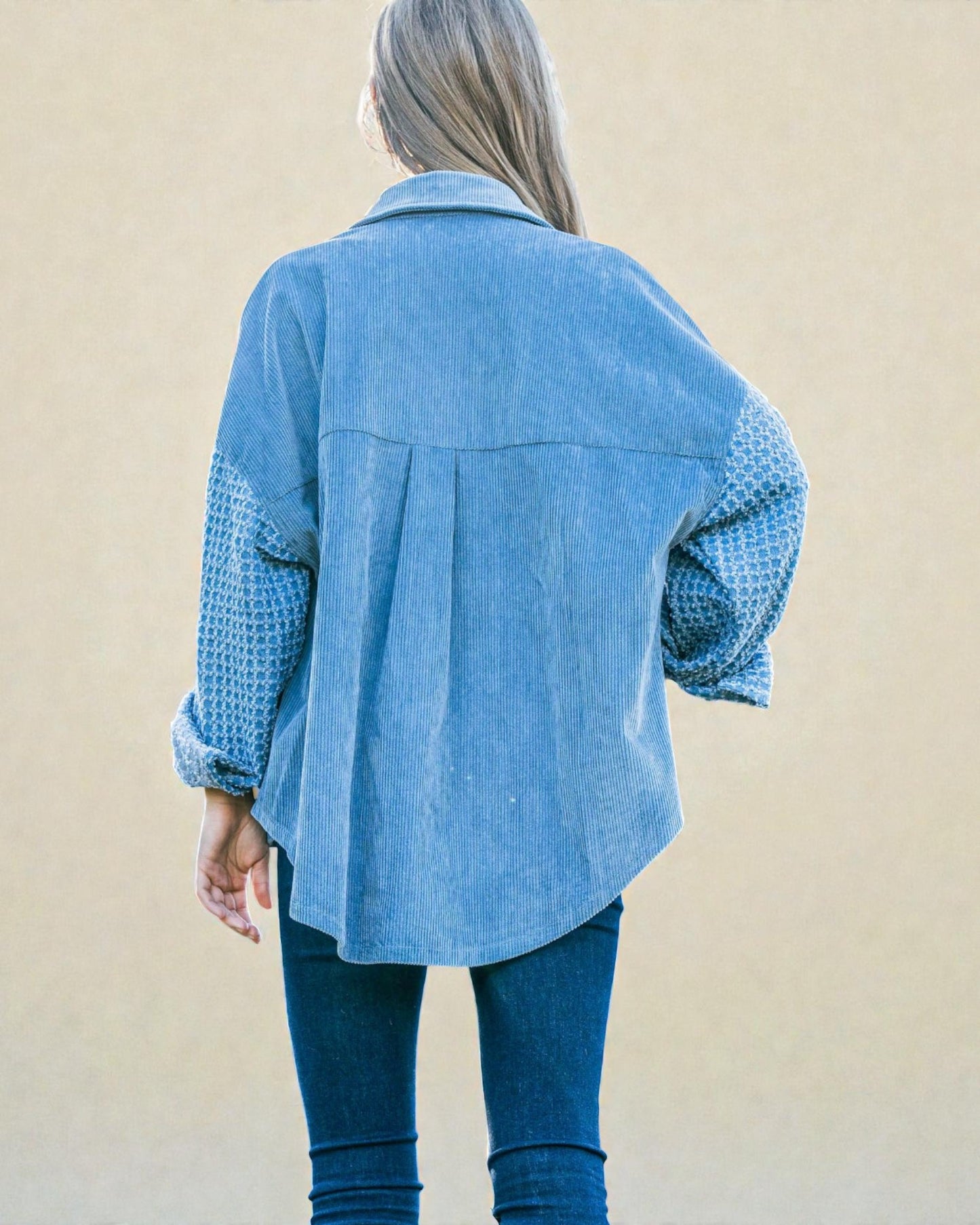 Person wearing a blue denim jacket with patterned sleeves against a beige background
