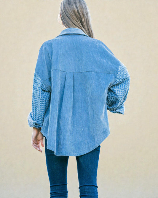 Person wearing a blue denim jacket with patterned sleeves against a beige background