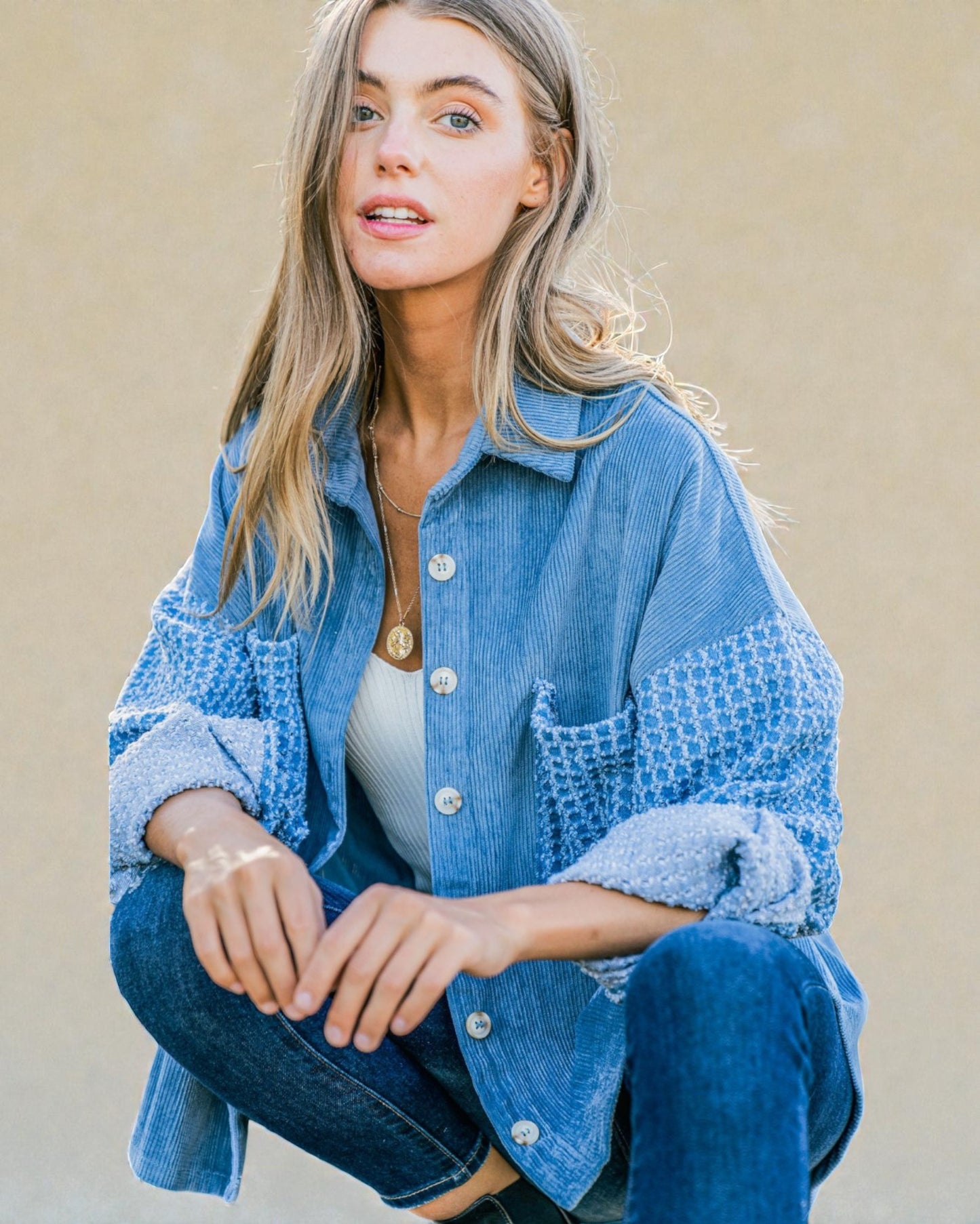 Woman wearing a blue denim jacket and jeans sitting against a beige background