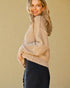 Woman wearing a beige sweater and dark jeans against a beige background