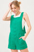 Woman wearing a green romper with a white shirt underneath on a light gray background