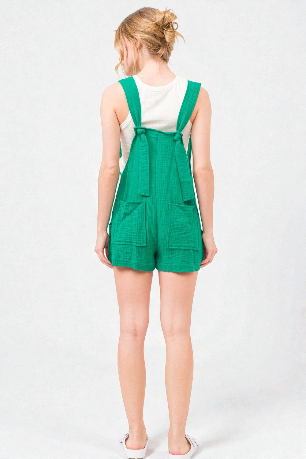 Person wearing a green overalls romper on a white background