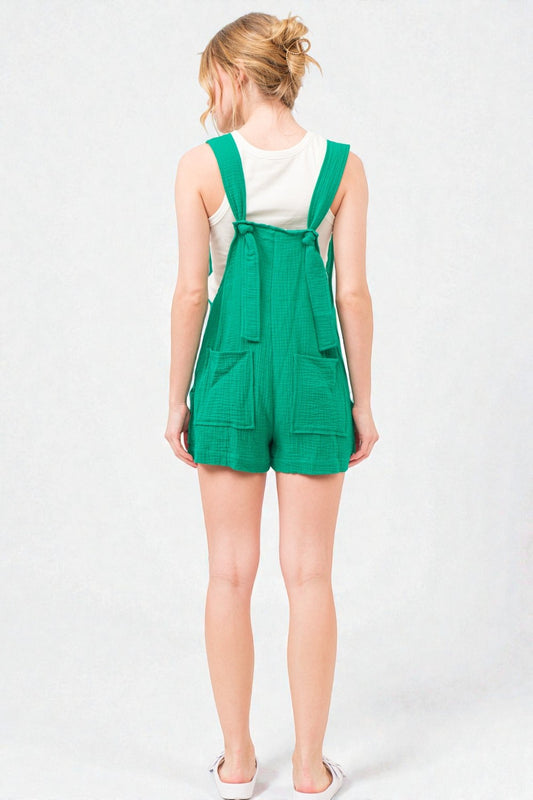 Person wearing a green overalls romper on a white background