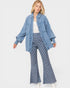 Woman wearing a blue denim jacket and checkered flared pants on a white background