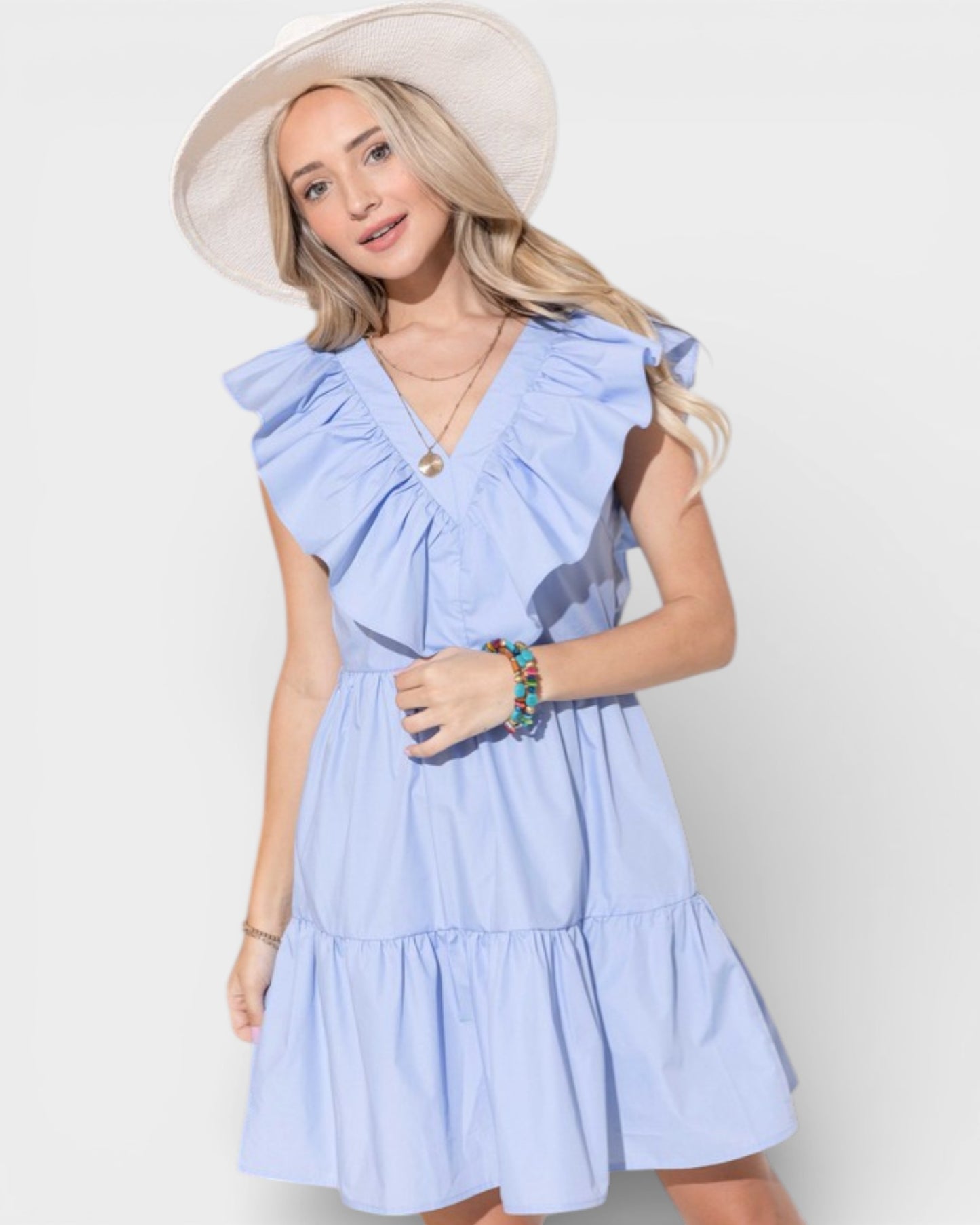 Woman wearing a light blue dress with ruffled sleeves and a white hat on a plain background
