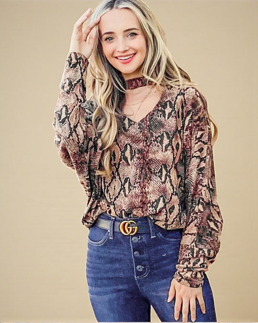 Woman wearing a snake print top and blue jeans with a beige background