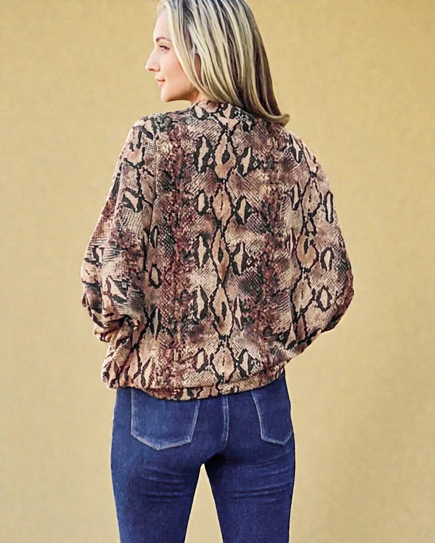 Person wearing a snake print blouse and blue jeans against a beige background