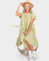 Woman wearing a light green dress with ruffled sleeves and a hat, holding a dried flower on a white background.
