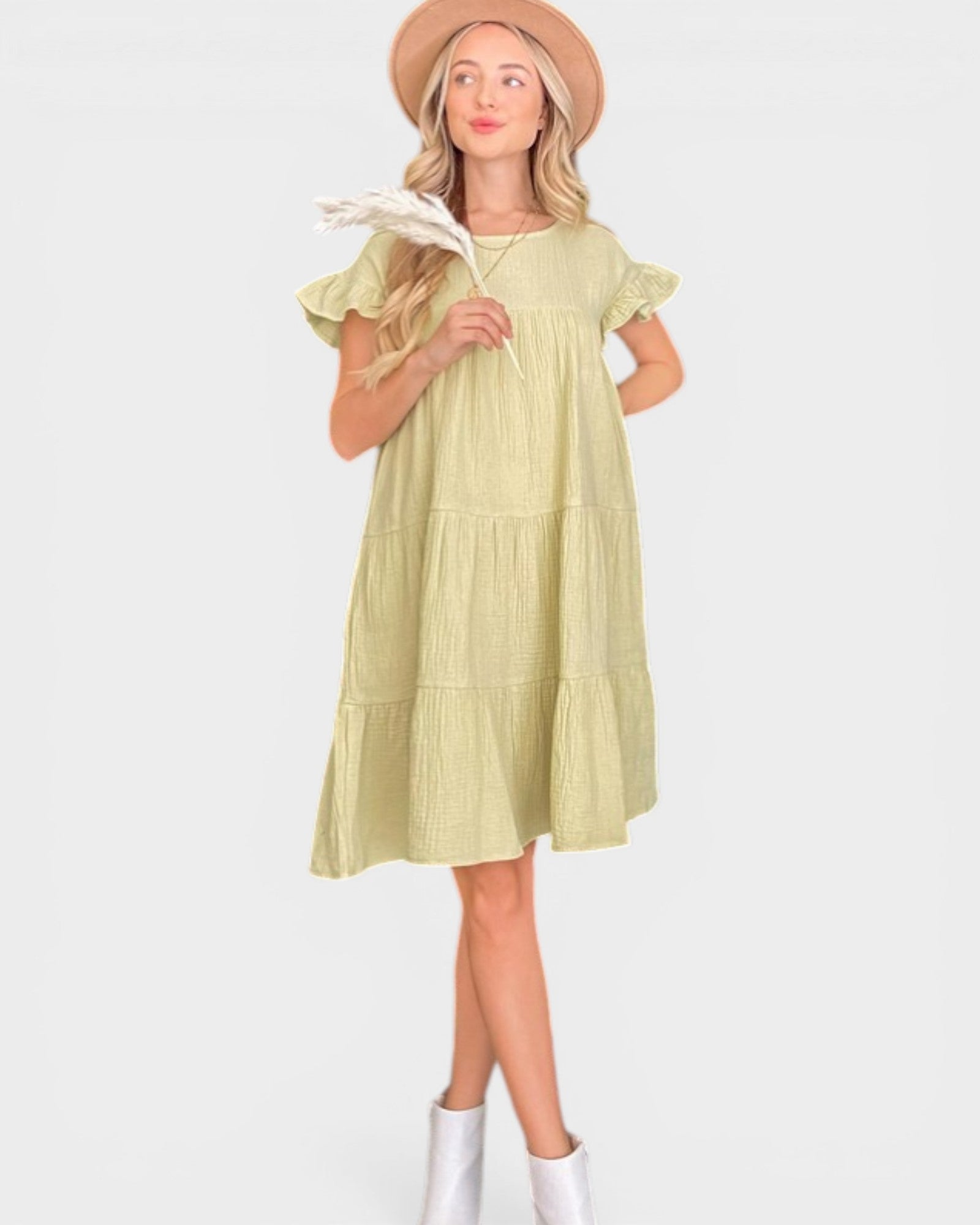 Woman wearing a light green dress with ruffled sleeves and white boots on a white background