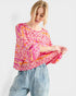 Woman wearing a colorful patterned top and jeans on a white background