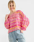 Woman wearing a colorful patterned top and jeans on a white background