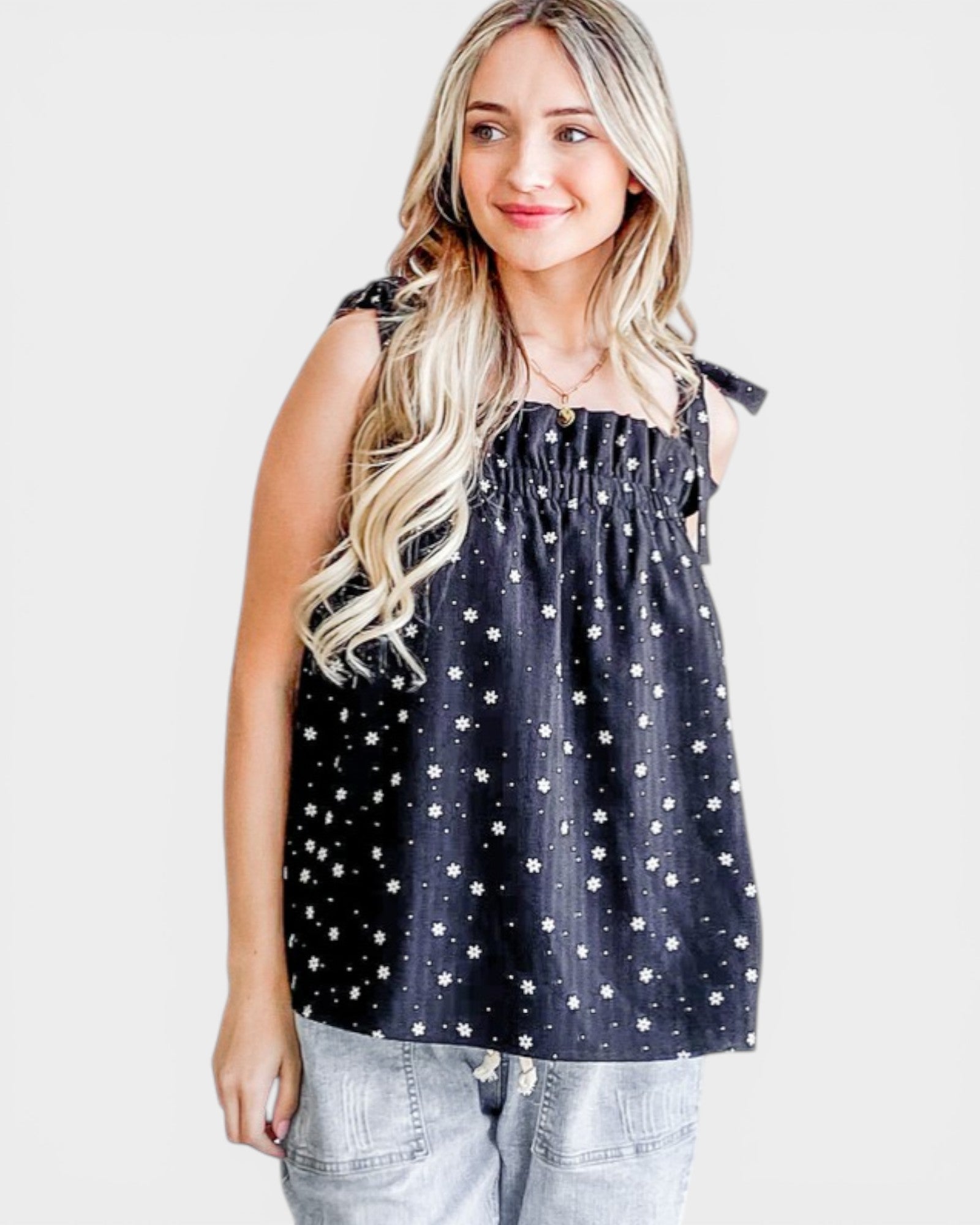 Woman wearing a black sleeveless top with white polka dots on a plain background