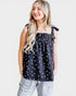Woman wearing a black sleeveless top with white polka dots and light gray pants on a white background
