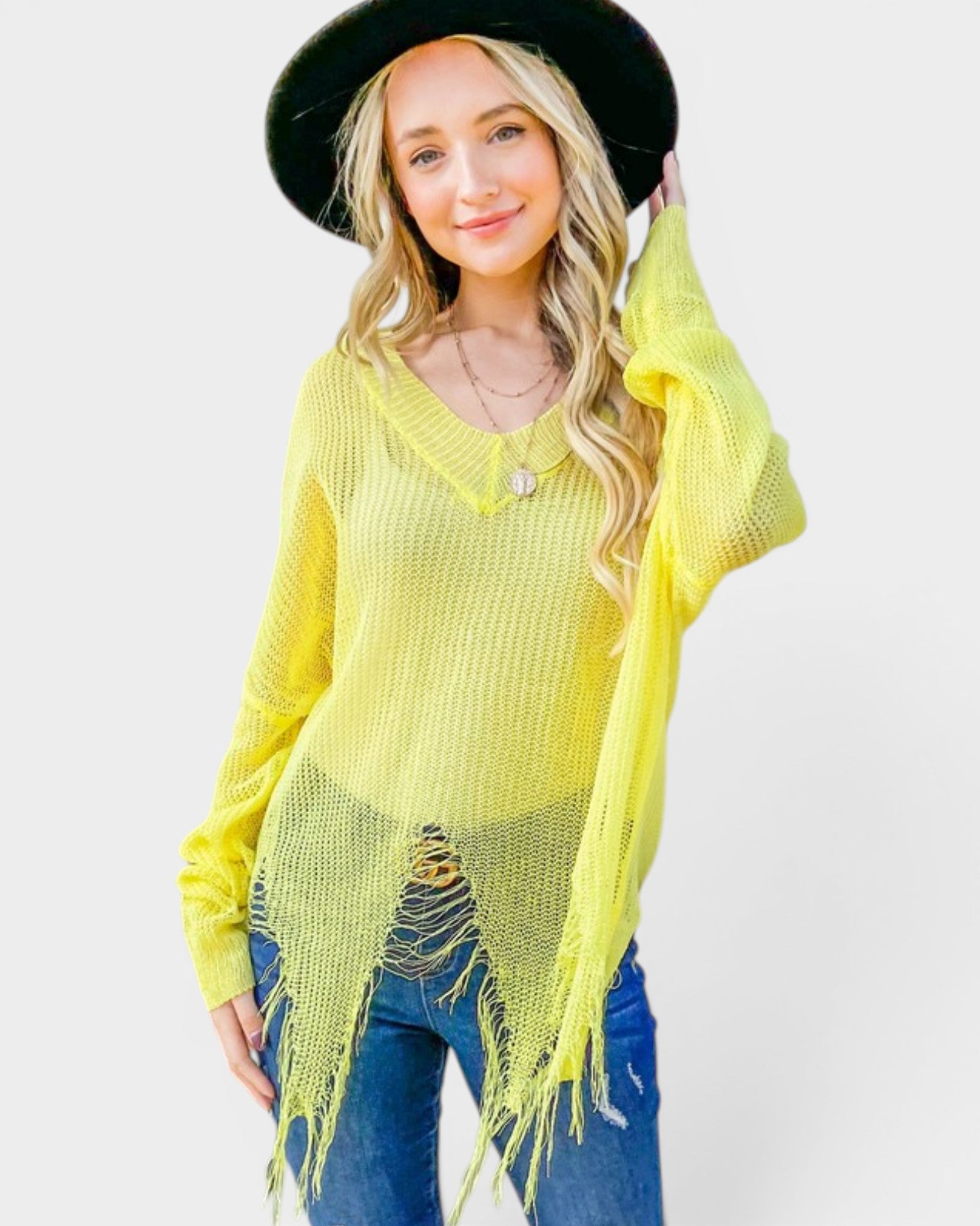 Woman wearing a bright yellow fringe sweater and black hat on a white background