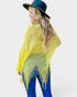 Woman wearing a bright yellow poncho and blue jeans with a white background