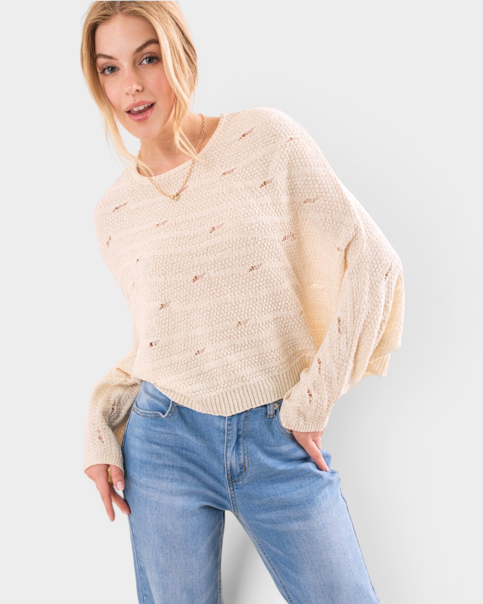 Woman wearing a beige sweater and blue jeans against a light gray background