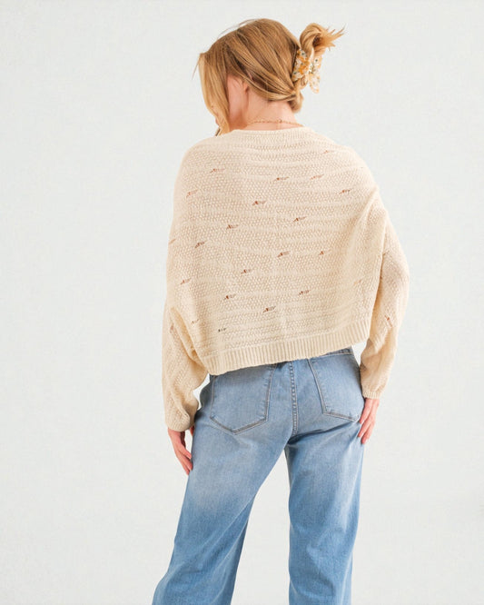 Person wearing a beige sweater and blue jeans on a plain background