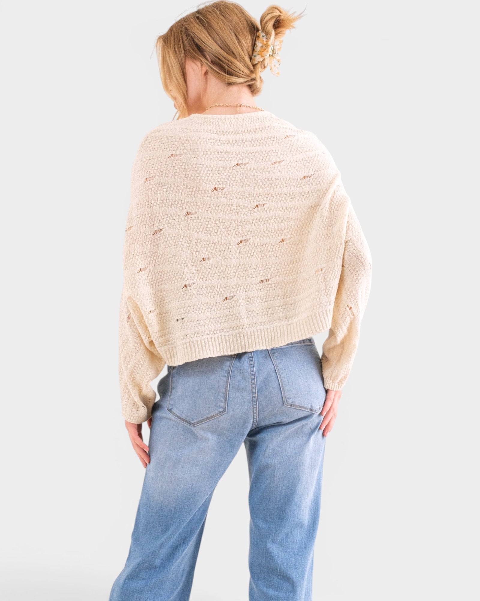 Person wearing a beige sweater and blue jeans on a white background