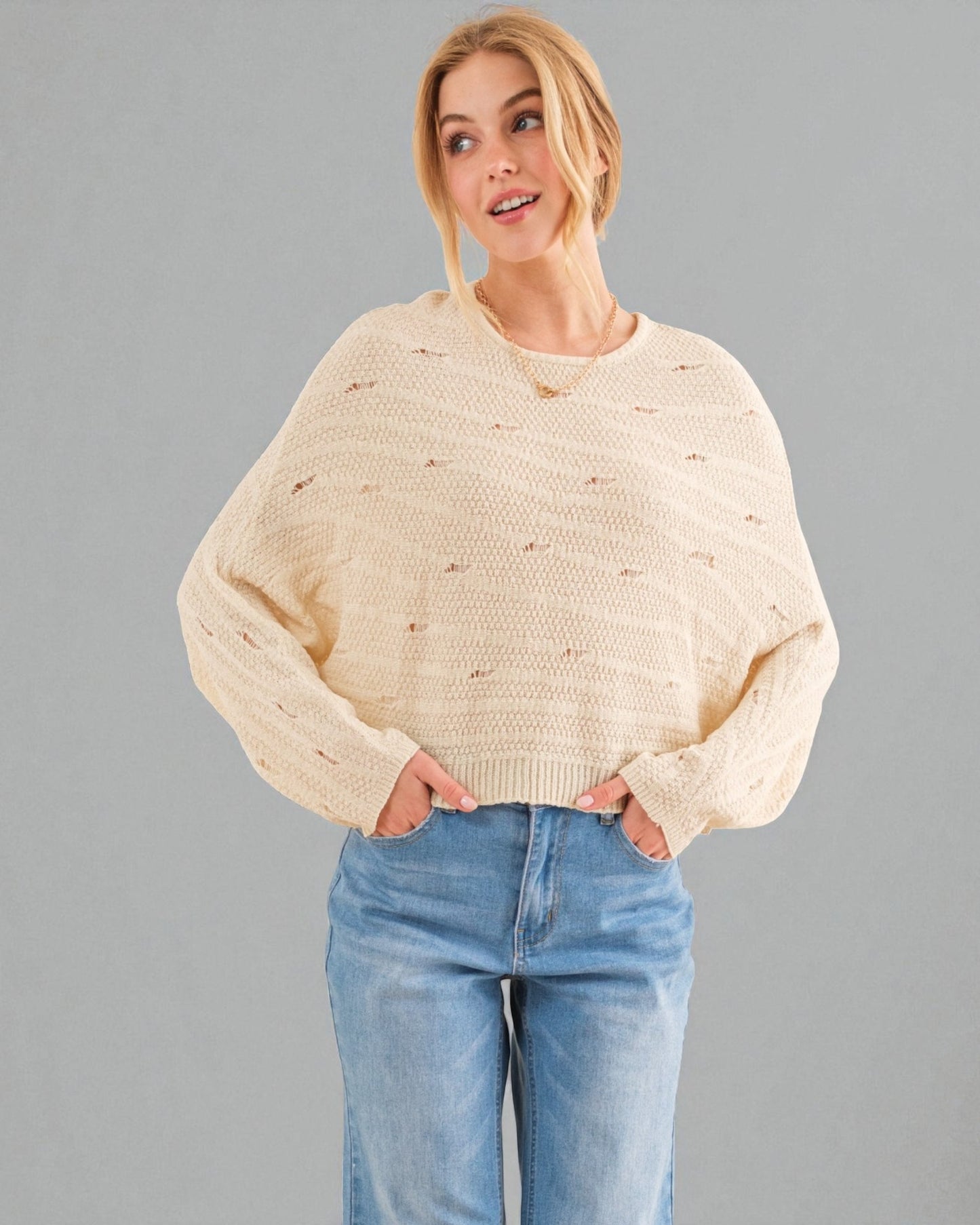 Woman wearing a beige sweater and blue jeans against a gray background