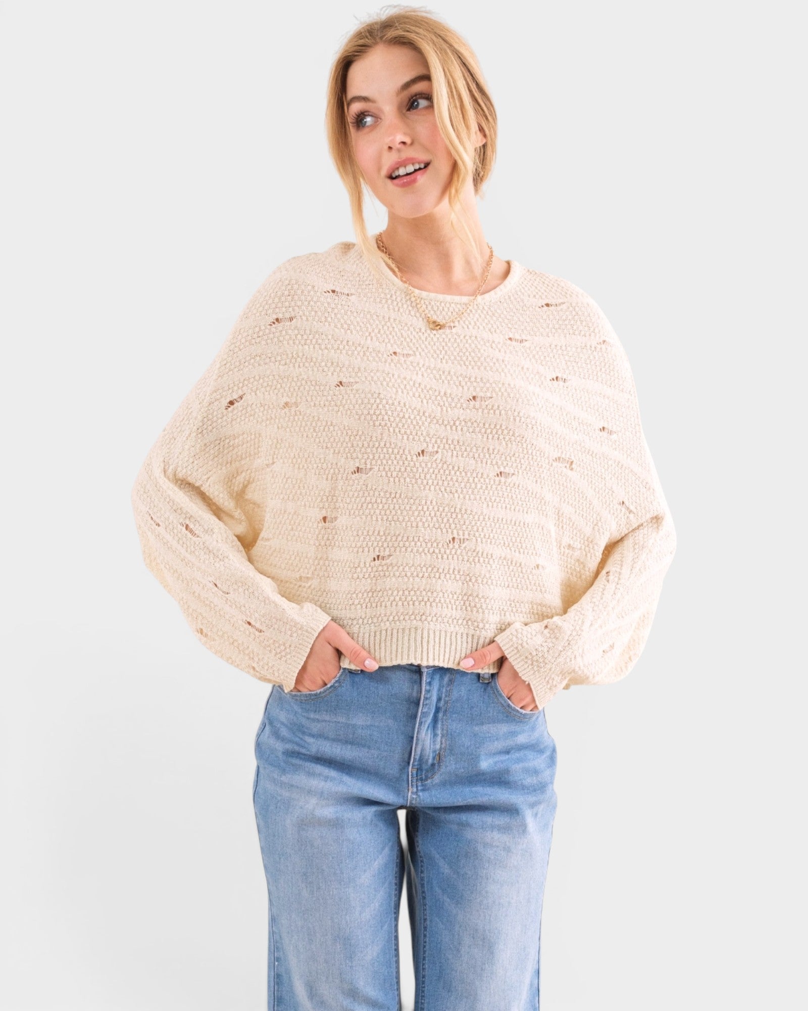 Woman wearing a beige sweater and blue jeans on a white background
