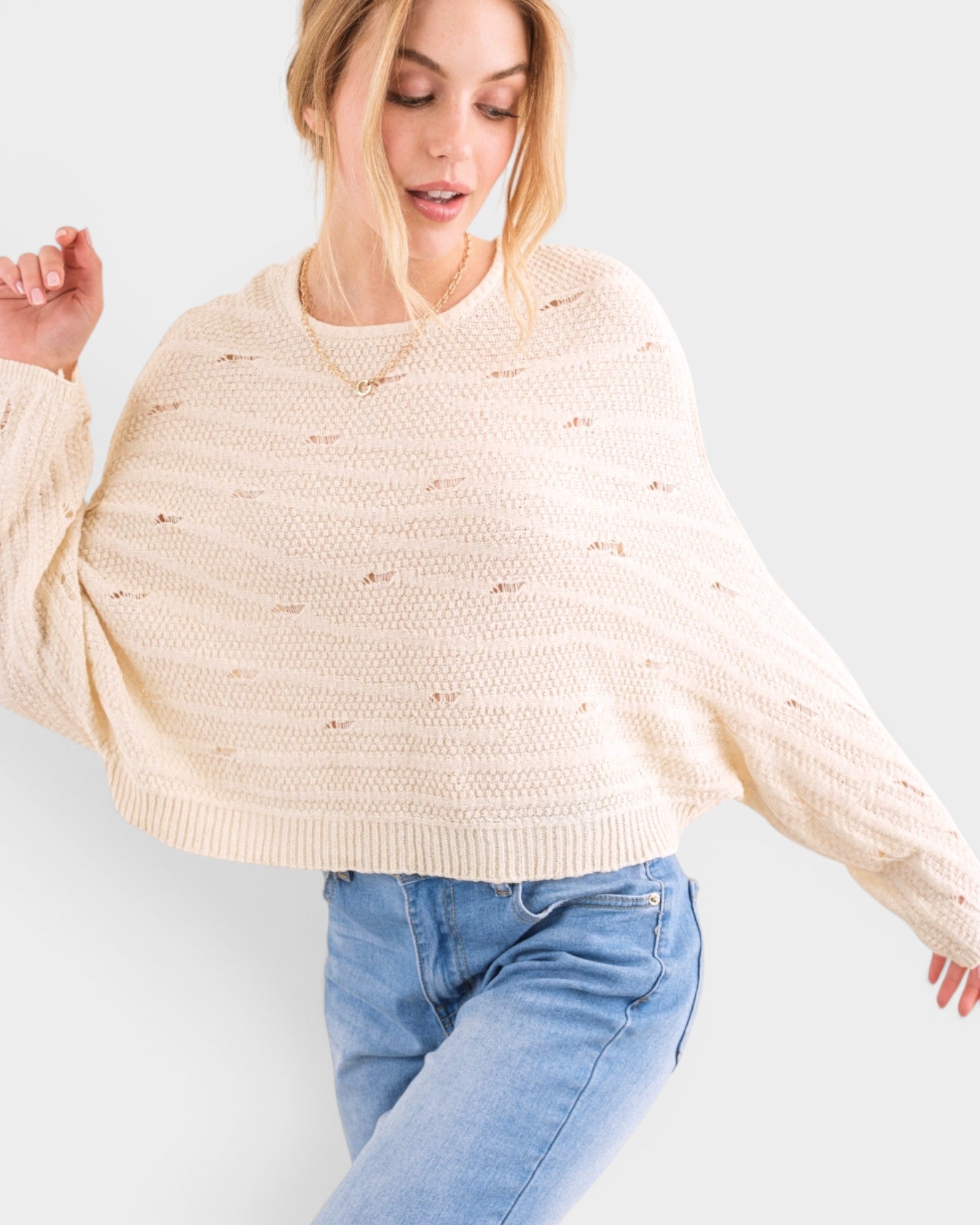 Woman wearing a beige sweater and blue jeans on a light gray background