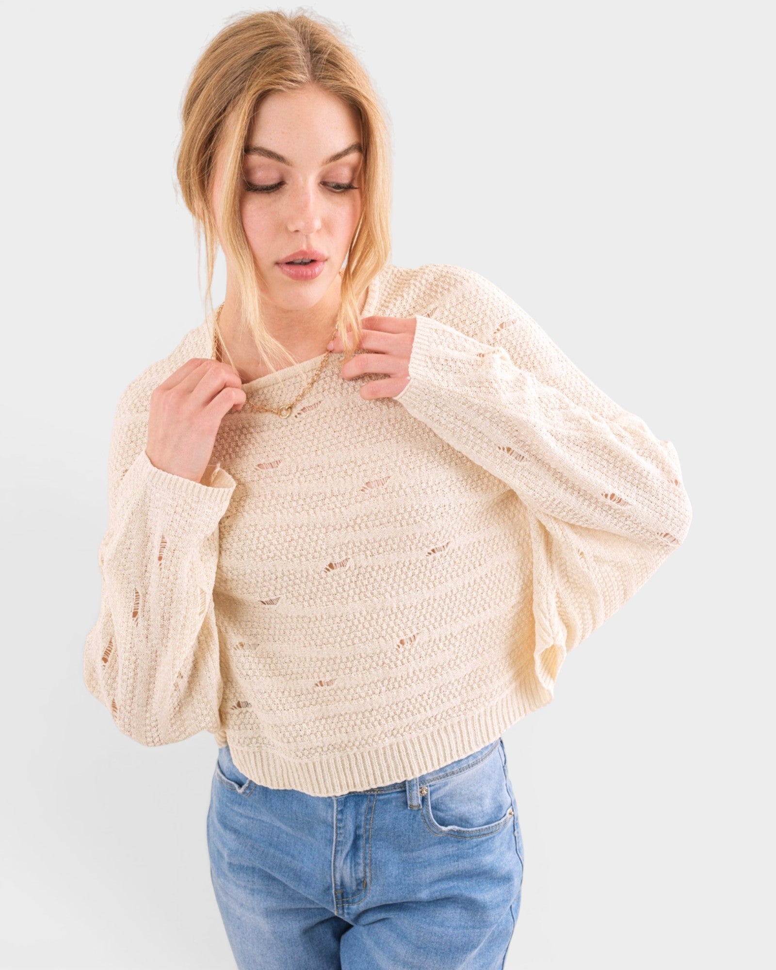 Woman wearing a beige sweater and blue jeans on a white background